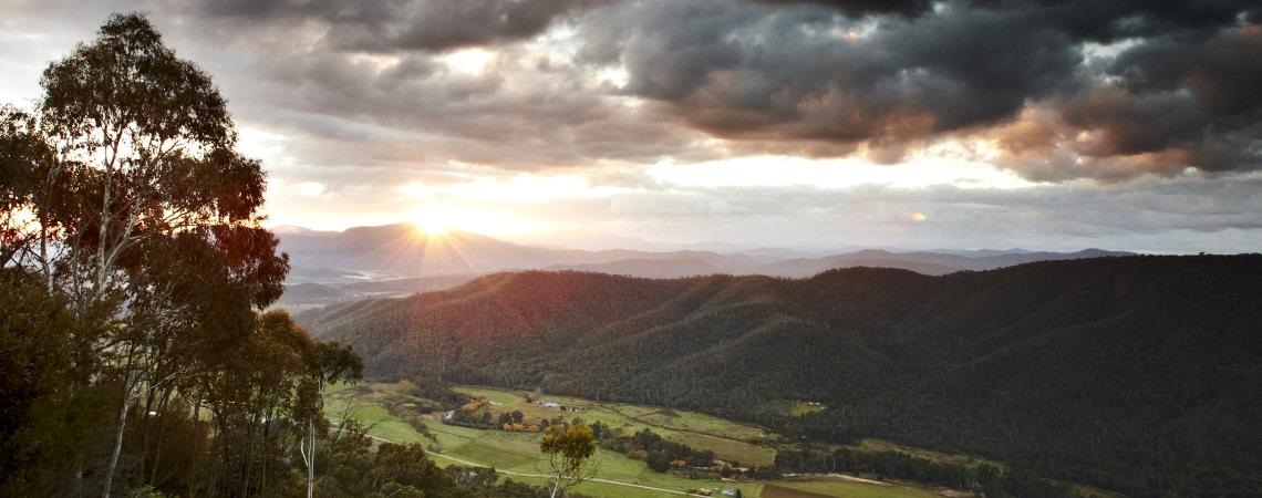 Views of Alpine National Park with sun rising over the mountains, farmland and vineyards in valley below